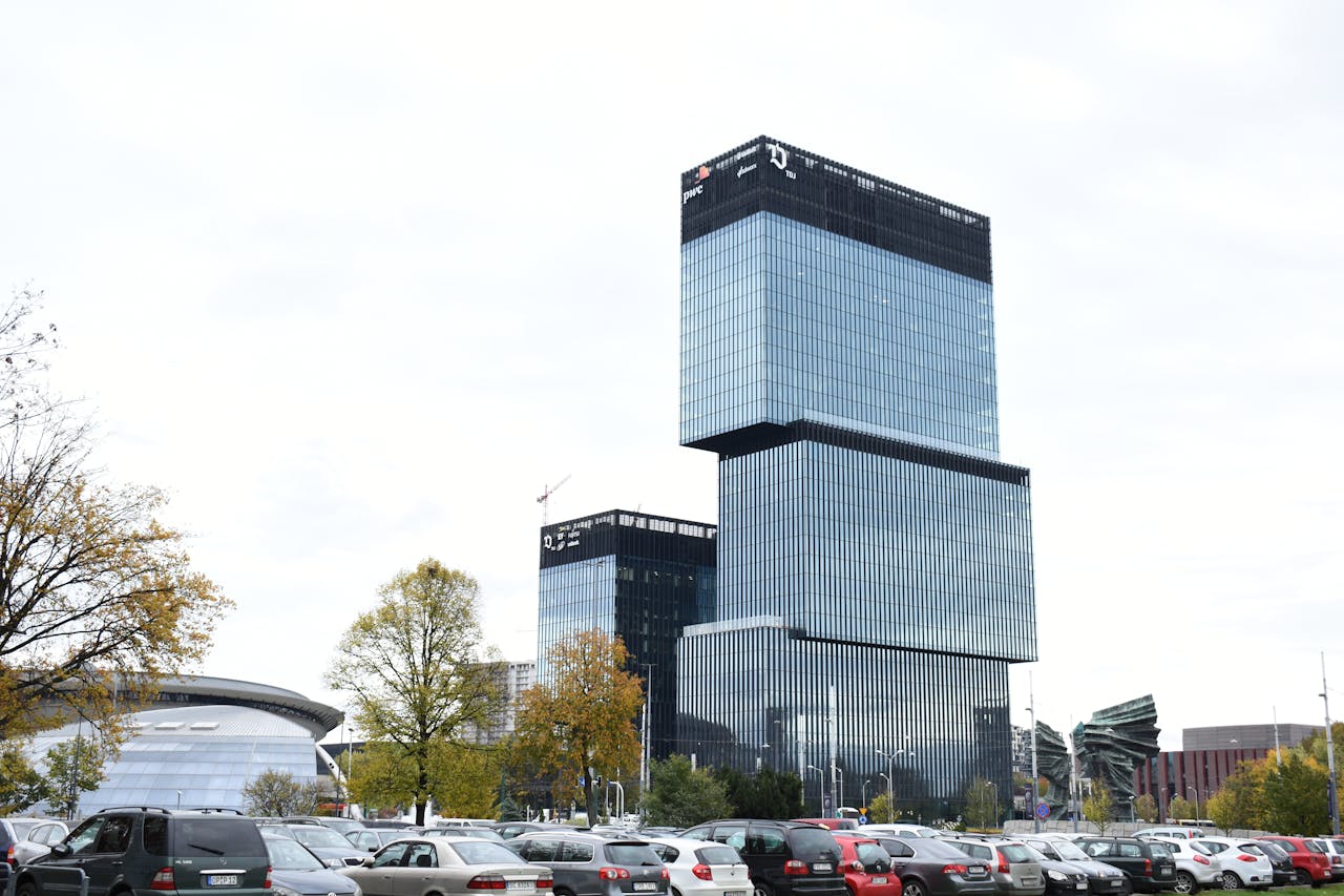 who-we-are Modern architecture of an office building in Katowice, Poland, with cars and trees in the foreground.