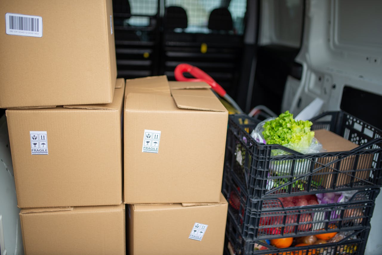 why-choose-us Cardboard boxes and fresh produce being prepared for delivery in a van, highlighting logistics and farm-to-table movement.